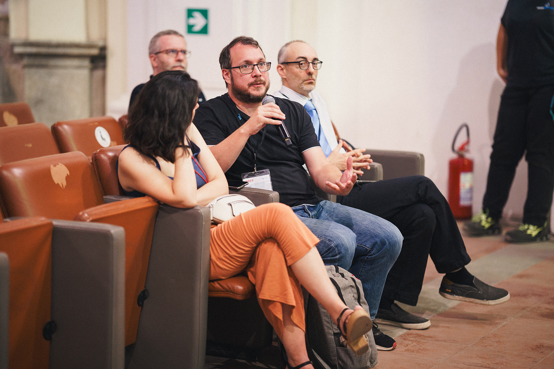 three people sitting in a row next to each other. The male in the middle holds a microphone and speaks into it.